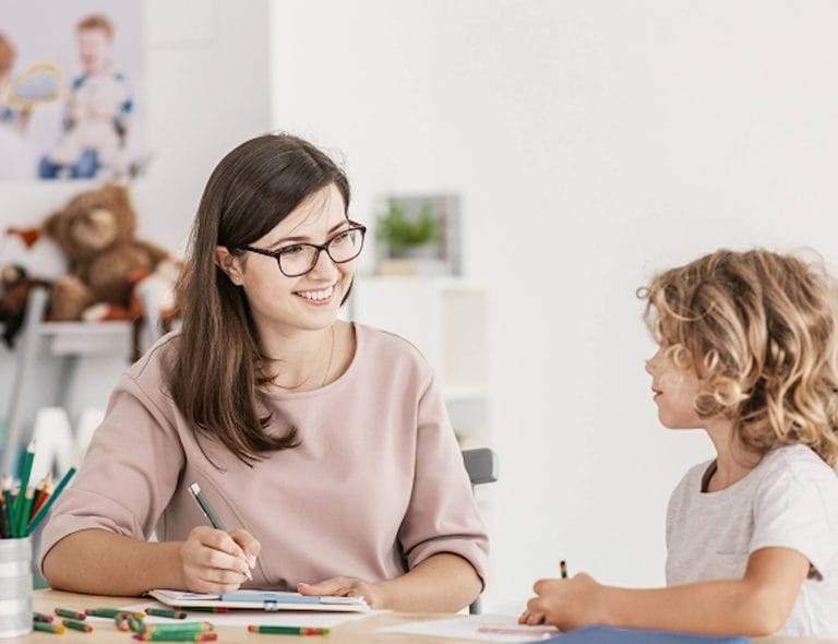 stock-photo-smiling-teacher-listening-to-autistic-boy-in-the-classroom-1205892301 1